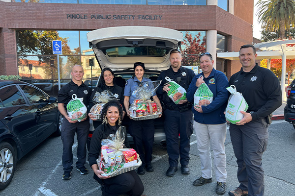 Pinole public safety facility with police in front with thanksgiving turkeys and other supplies packaged as gifts for community members