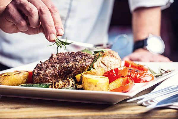 Chef in hotel or restaurant kitchen cooking Prepared beef steak with vegetable decoration.