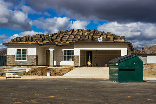 Dumpster on the street in front of a ranch style home being built