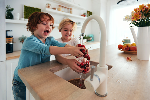 happy kids washing cherries under tap water at the kitchen