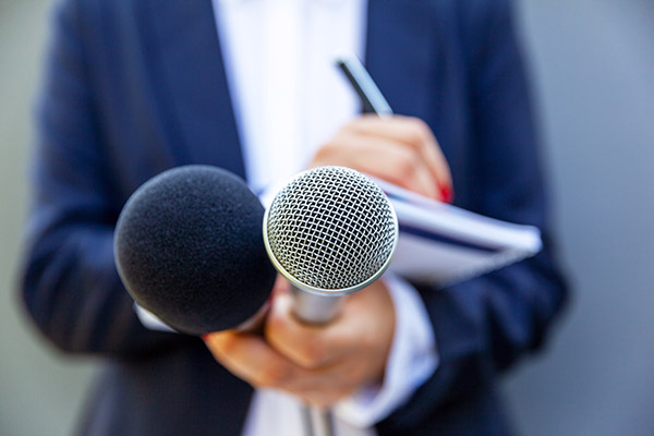Journalist in suit holds notepad and microphones.