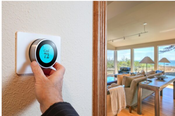 Hand adjusting smart thermostat with living room in background