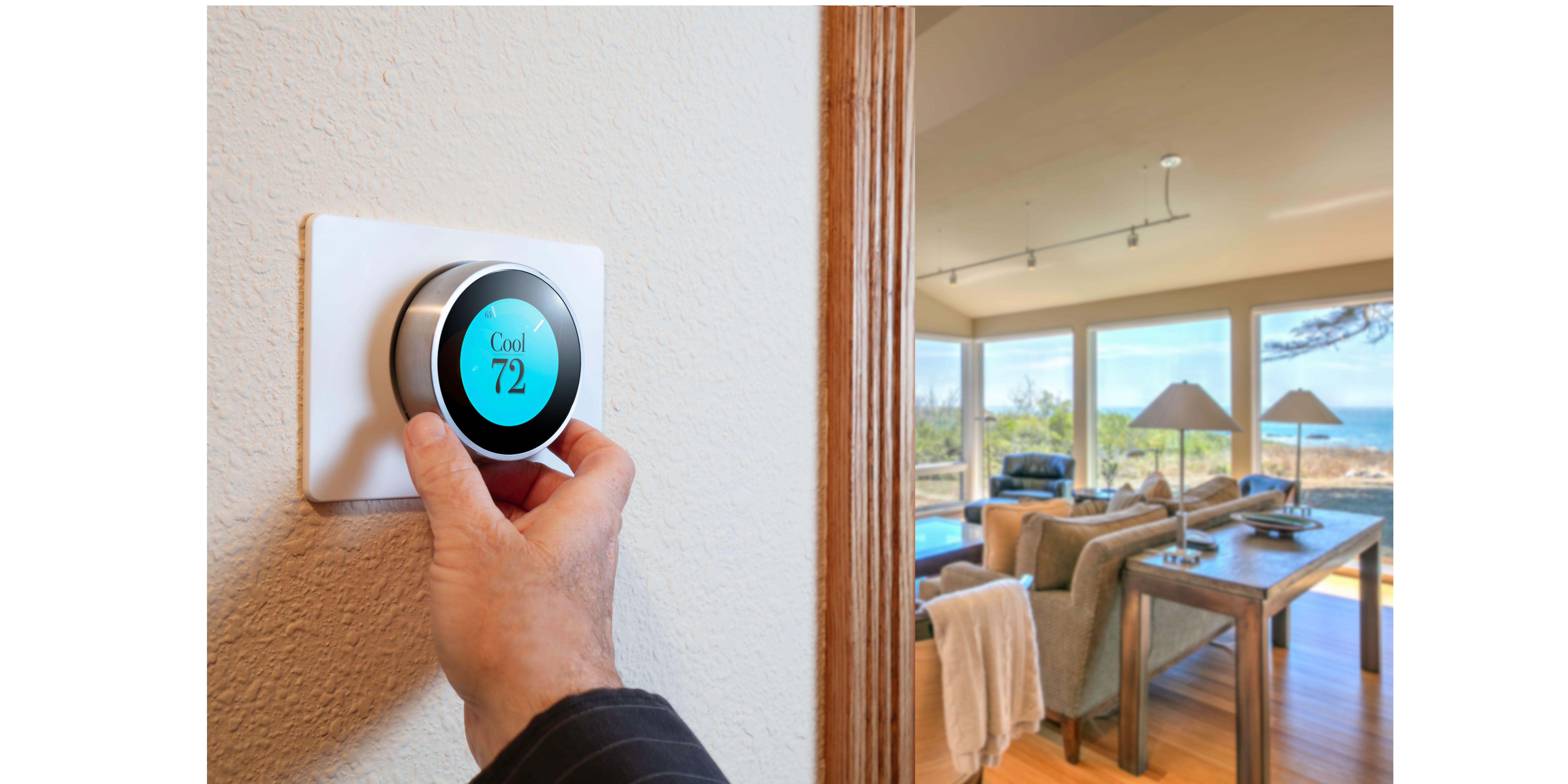 Hand adjusting smart thermostat with living room in background