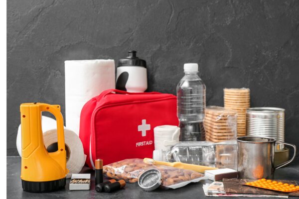 Emergency preparedness items (flashlight, first aid kit, water and other supplies) on a table with a dark grey wall.
