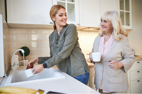 Two people standing in a kitchen, with one person rinsing a mug at the sink while the other person holds a mug nearby